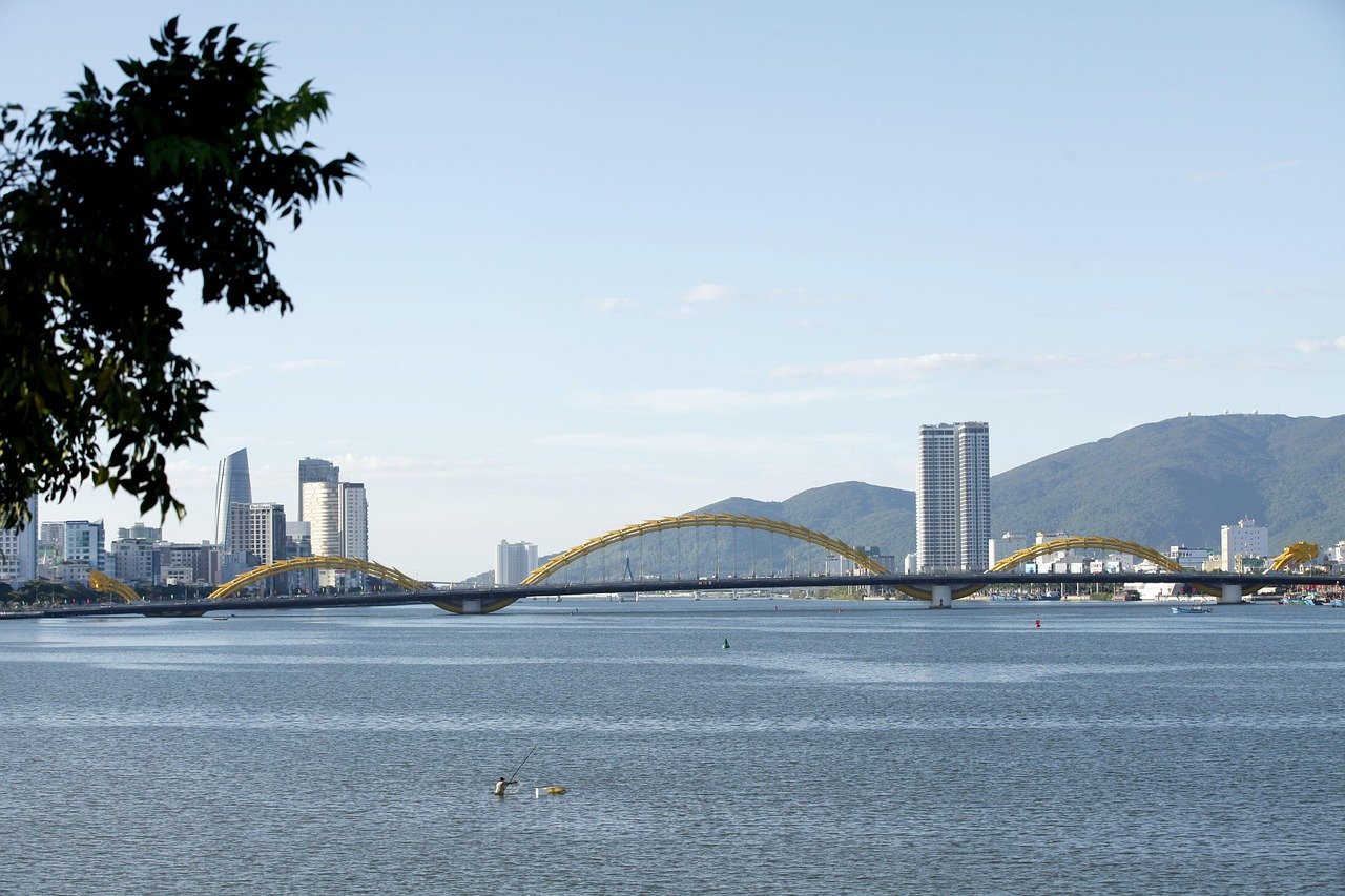 Scenic view of Dragon Bridge over Han River with city skyline and mountains in Da Nang, Vietnam under clear blue sky