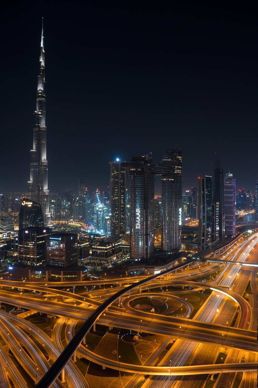 Night view of Dubai city skyline with illuminated Burj Khalifa and busy highway interchange with light trails