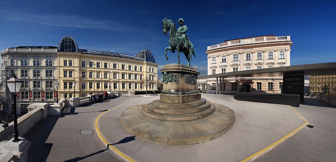 Equestrian statue in front of historic buildings and Albertina Museum in Vienna under clear blue sky
