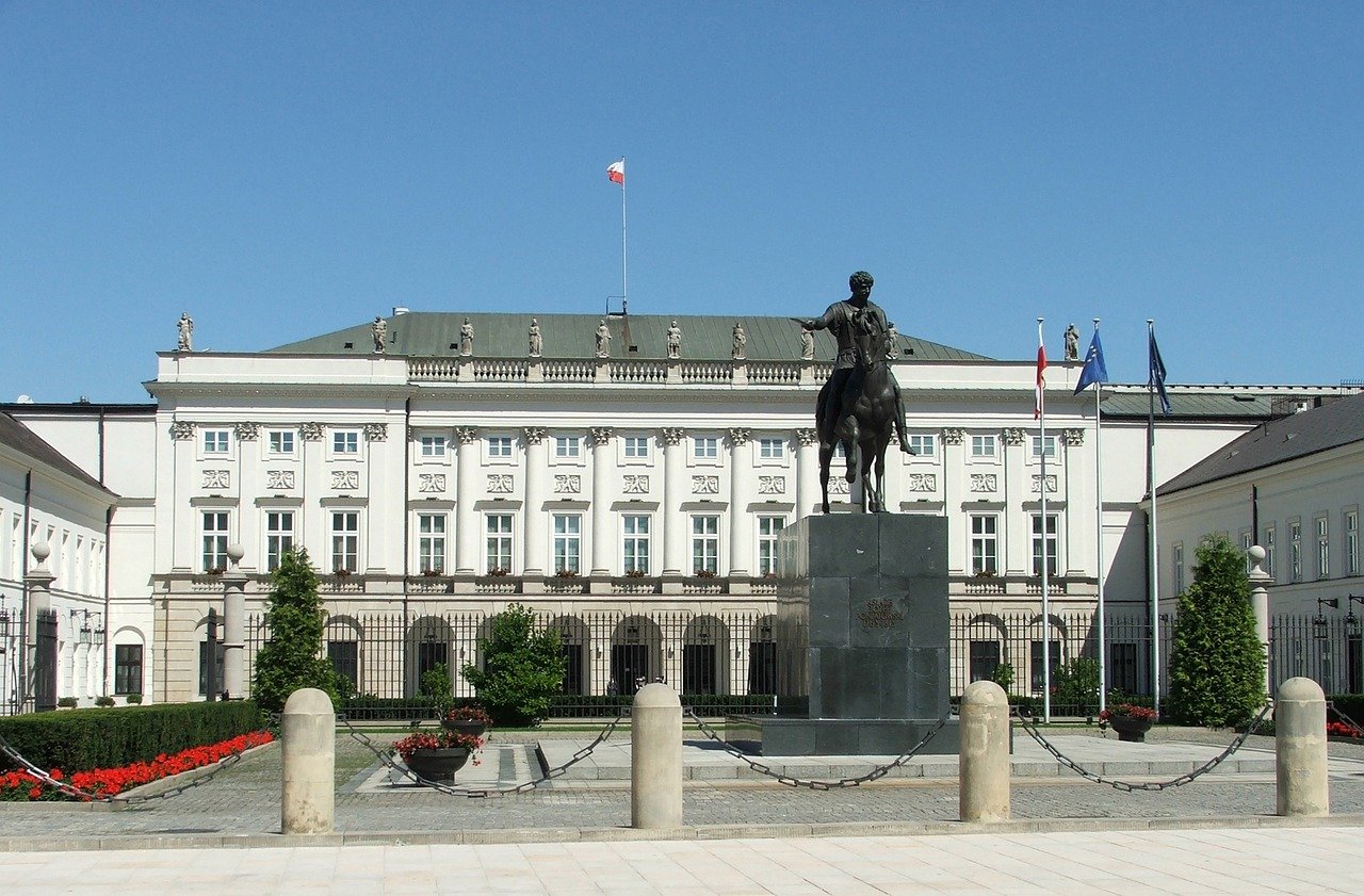 Equestrian statue in front of a historic white government building with Polish flag and clear blue sky