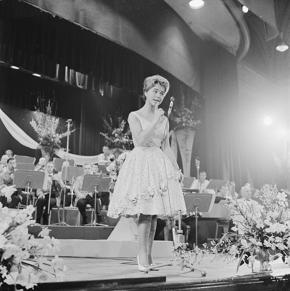 Young woman singing on stage with orchestra in the background during a vintage concert performance