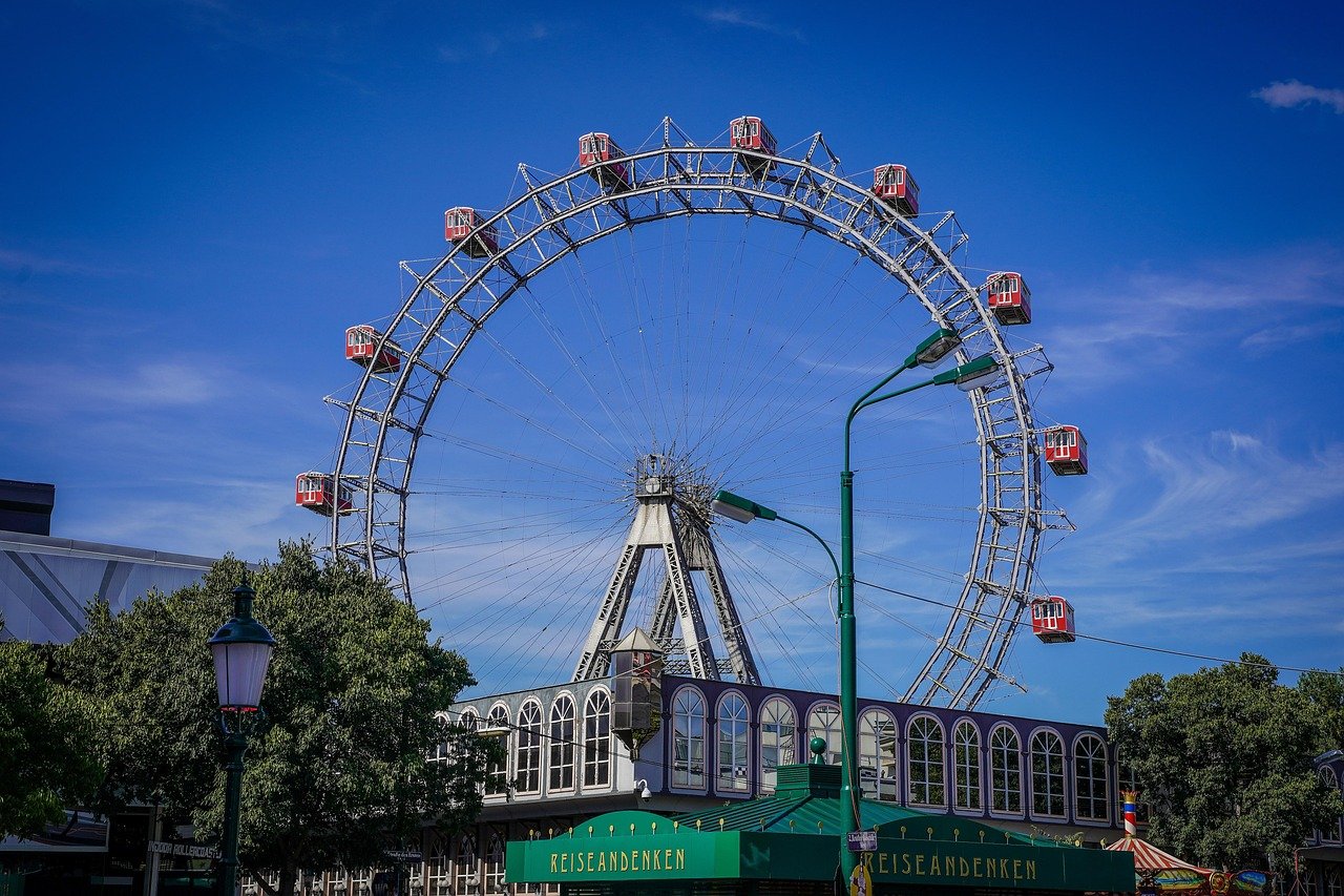 Large Ferris wheel with red cabins at an amusement park under a clear blue sky during daytime