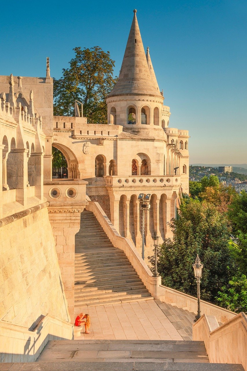 Fisherman's Bastion in Budapest with stone stairs and a person sitting, historic architecture under clear blue sky