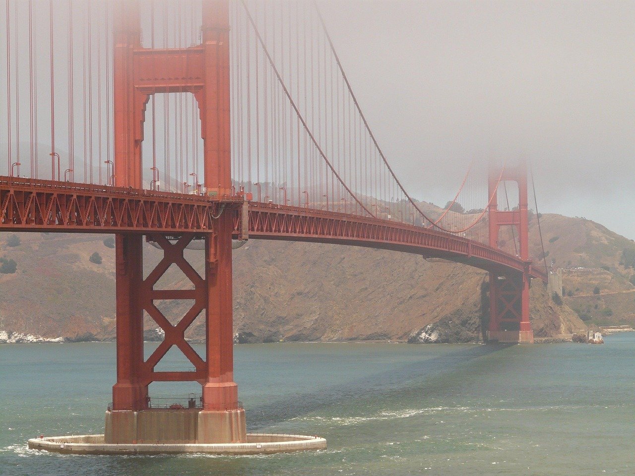 Golden Gate Bridge in San Francisco partially covered by fog over the bay with hills in the background