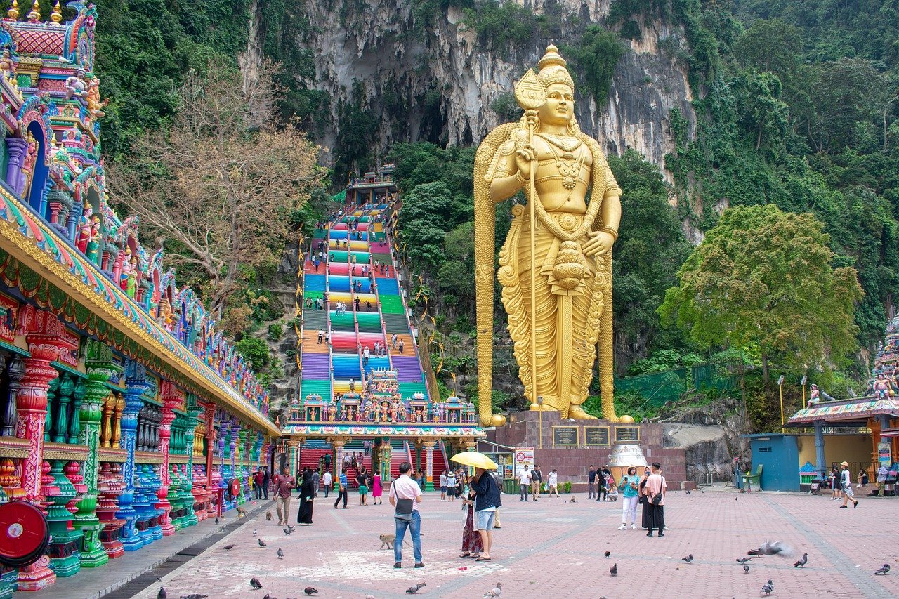 Large golden statue of Lord Murugan at Batu Caves with colorful stairs and temple entrance in Malaysia