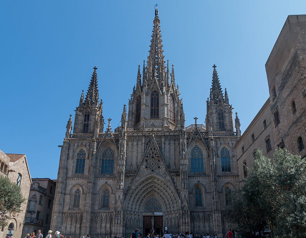 Gothic cathedral with spires and tourists Gothic cathedral facade with intricate spires and detailed stone carvings under clear blue sky, crowded with tourists