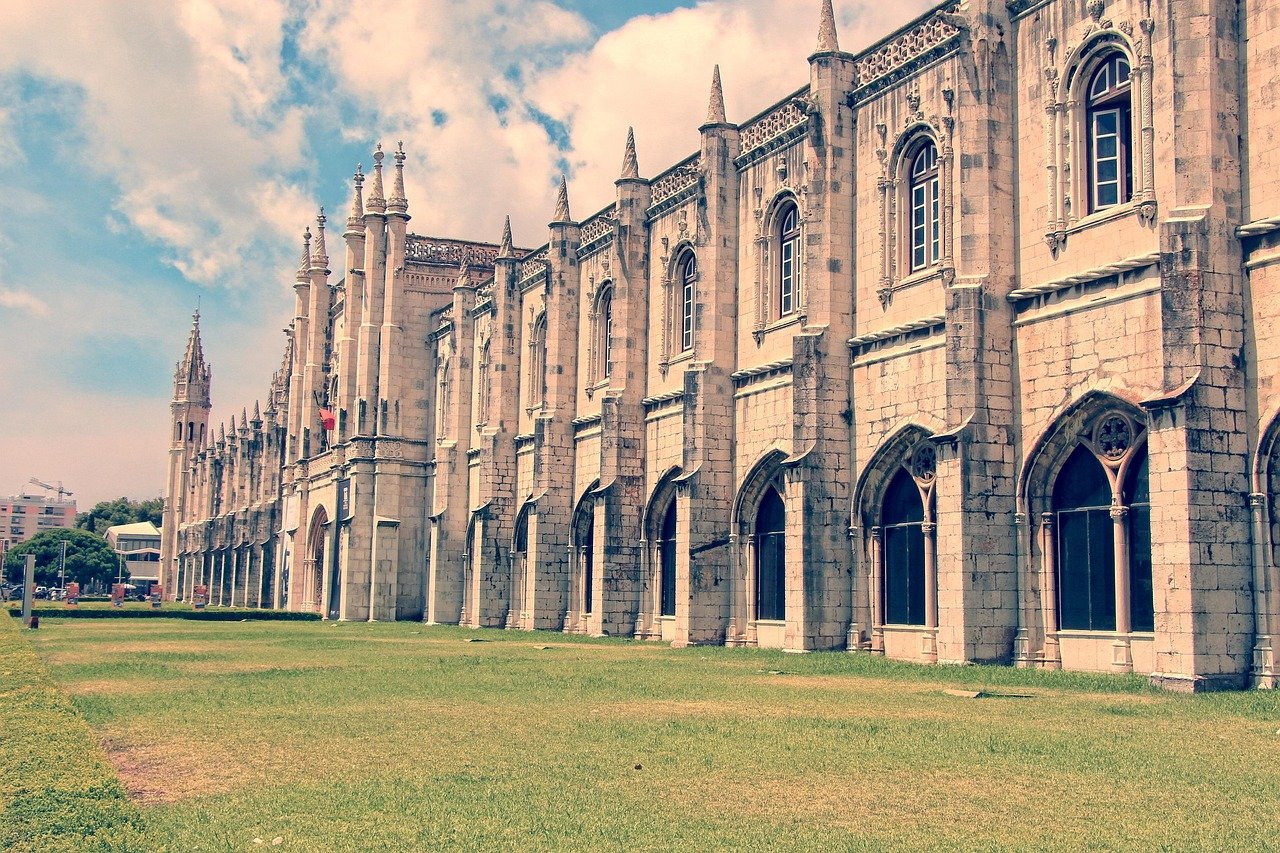 Historic Gothic-style monastery building with pointed arches and spires under a blue sky with clouds