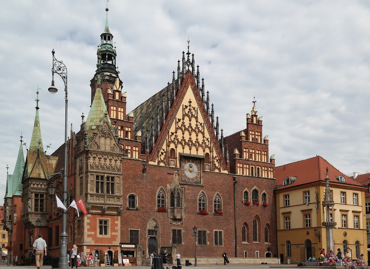 Historic Gothic-style town hall with ornate clock tower and red brick facade in a European city square under cloudy sky
