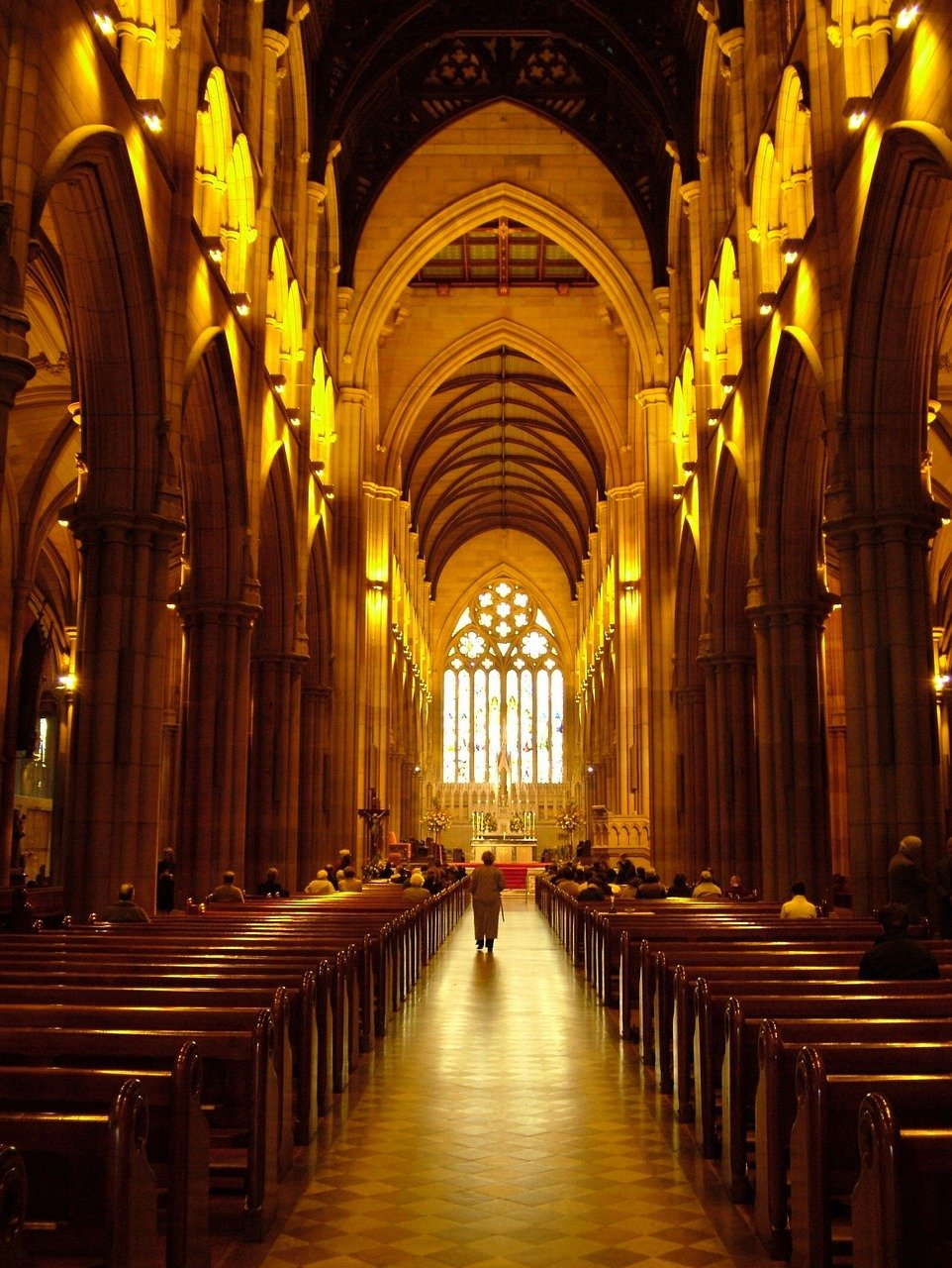 Interior view of a grand cathedral with high arches, wooden pews, and a glowing altar with stained glass windows