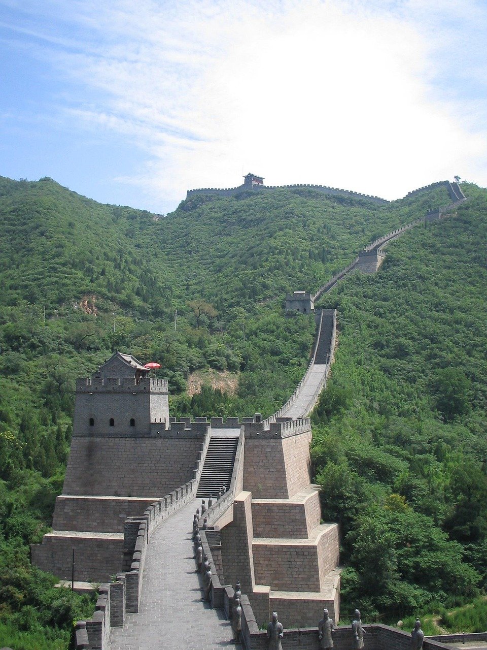 The Great Wall of China winding over green hills under a blue sky, showcasing ancient stone architecture and watchtowers.