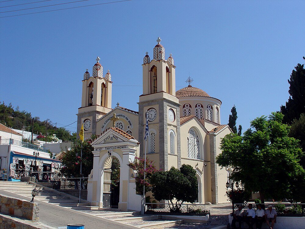 Greek Orthodox Church with Twin Bell Towers Greek Orthodox church with twin bell towers and clock faces under clear blue sky in a sunny village setting