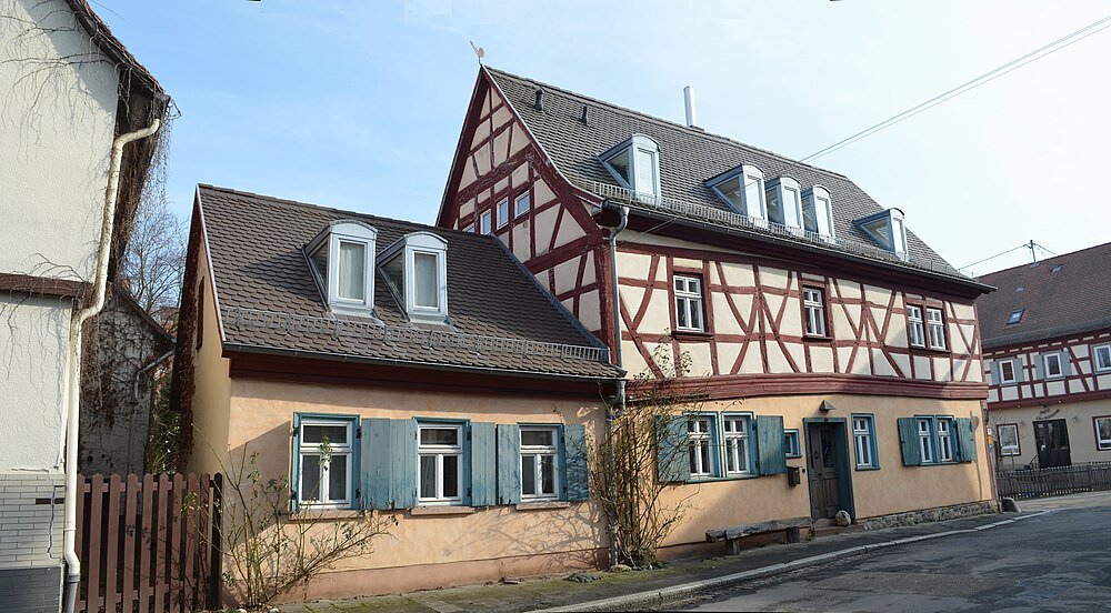 Traditional half-timbered house with blue shutters and steep roof in a quiet European village street under clear sky