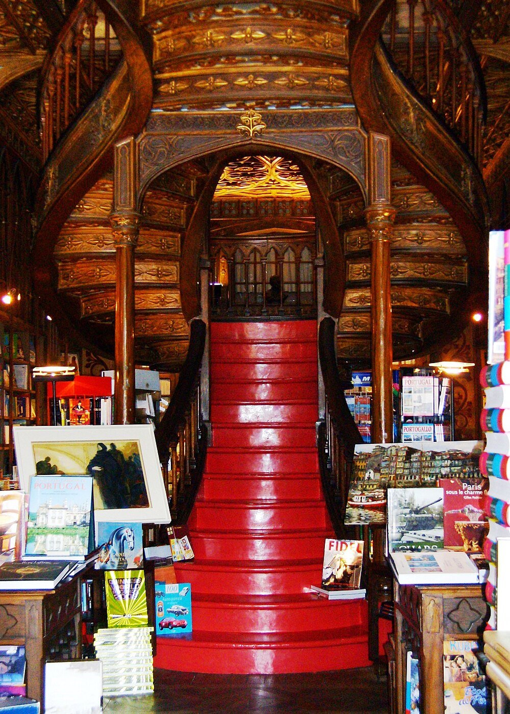 Intricately carved wooden spiral staircase with red steps inside a historic bookstore filled with books and artwork