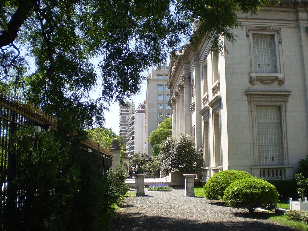 Historic building with columns and green garden Elegant historic building with classical columns and lush greenery in an urban park setting under bright daylight