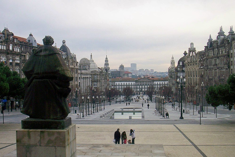 Historic city square with statue and buildings Wide city square with historic buildings, statue, and people walking in an urban European setting under cloudy sky