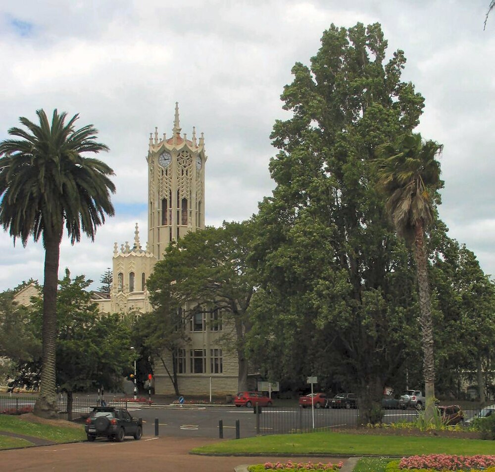 Historic clock tower with palm trees and greenery Historic clock tower building surrounded by tall palm trees and lush greenery under a cloudy sky