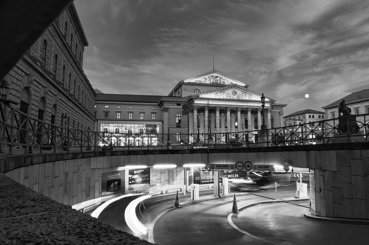 Black and white photo of historic European building with columns and curved road with light trails at dusk