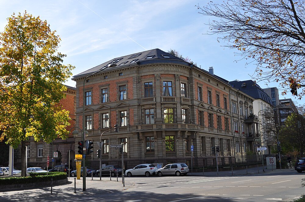 Historic Galeriehaus building with classic architecture and parked cars on a sunny day in an urban setting