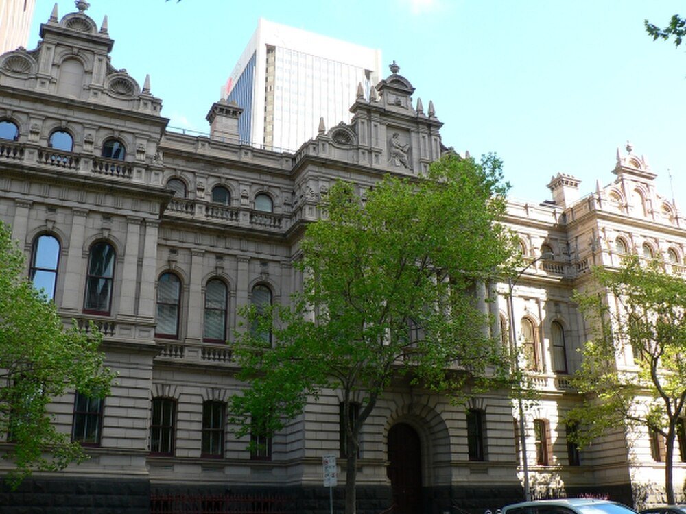 Historic classical government building with trees Historic government building with classical architecture and arched windows partially obscured by green trees in urban setting