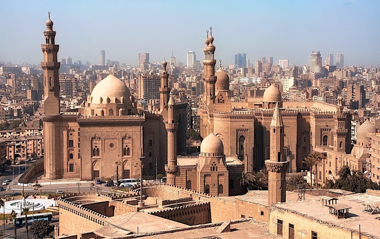 Historic Islamic architecture with multiple domes and minarets in a densely built urban cityscape under clear sky