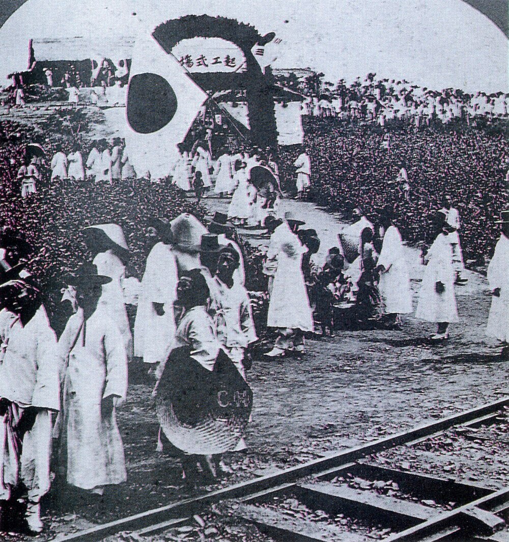 Historic Korean workers near railway and windmill Historic black and white photo of Korean workers in traditional clothing gathered near railway tracks and a windmill.