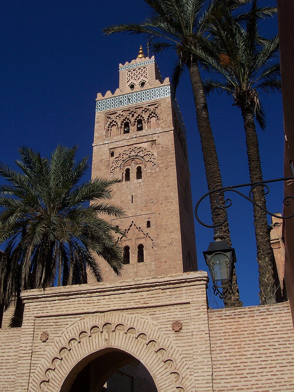 Historic mosque tower with palm trees in Marrakech Tall historic mosque tower with intricate stone carvings and palm trees under clear blue sky in Marrakech Morocco