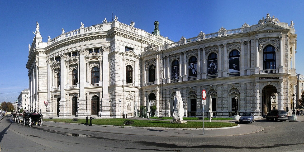 Historic white stone opera house with classical architecture and sculptures under clear blue sky in urban setting