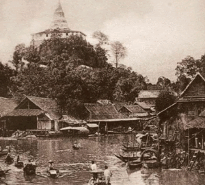 Historic riverside village with hilltop temple Historic riverside village with traditional wooden houses and boats near a hilltop temple in Southeast Asia