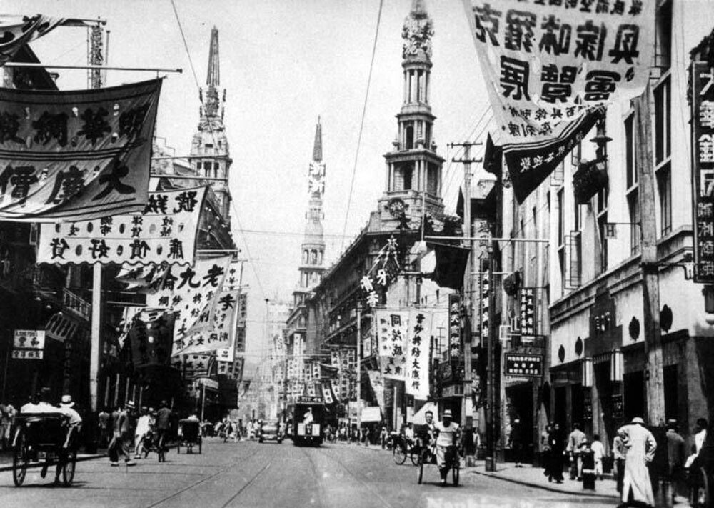 Historic black and white street scene in early 20th century Shanghai with traditional Chinese banners and rickshaws