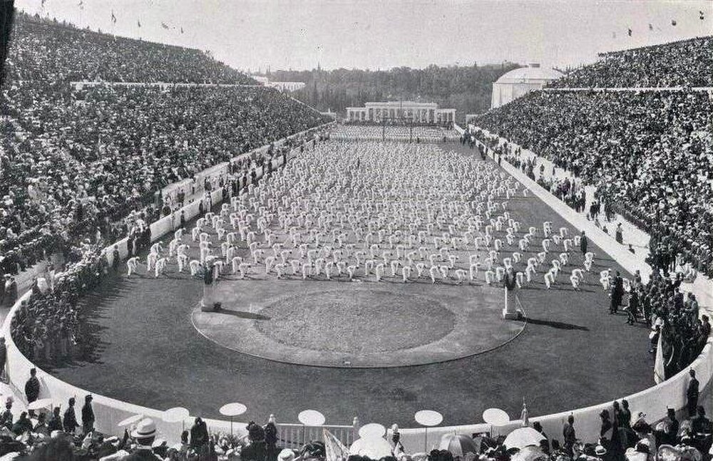 Historic stadium with synchronized athletes and crowd Historic black and white photo of a large stadium filled with spectators and athletes performing synchronized exercises on the field