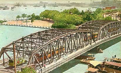 Historic steel railway bridge over river with trains Historic steel truss railway bridge over river with trains and boats, surrounded by greenery and cityscape in background