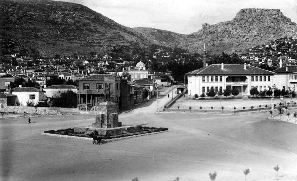 Historic town square with statue and mountains Historic black and white photo of a town square with a statue, traditional buildings, and mountainous background