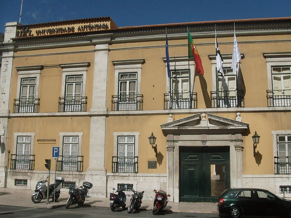 Historic university building facade with flags and vehicles Facade of a historic university building with flags and parked motorcycles and cars in front under clear sky