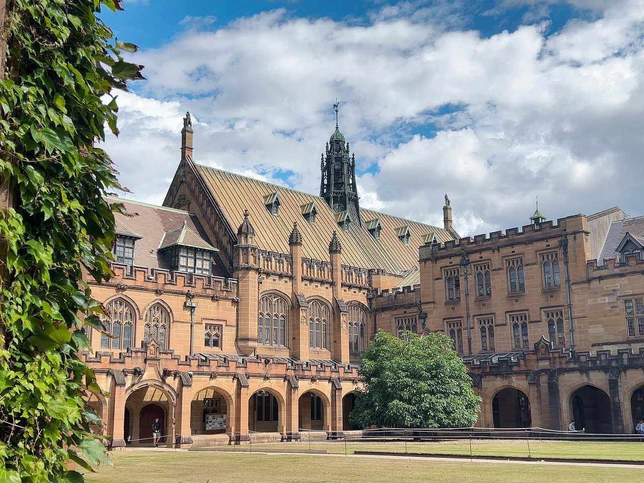Historic sandstone university building with arched windows and green ivy under a partly cloudy sky