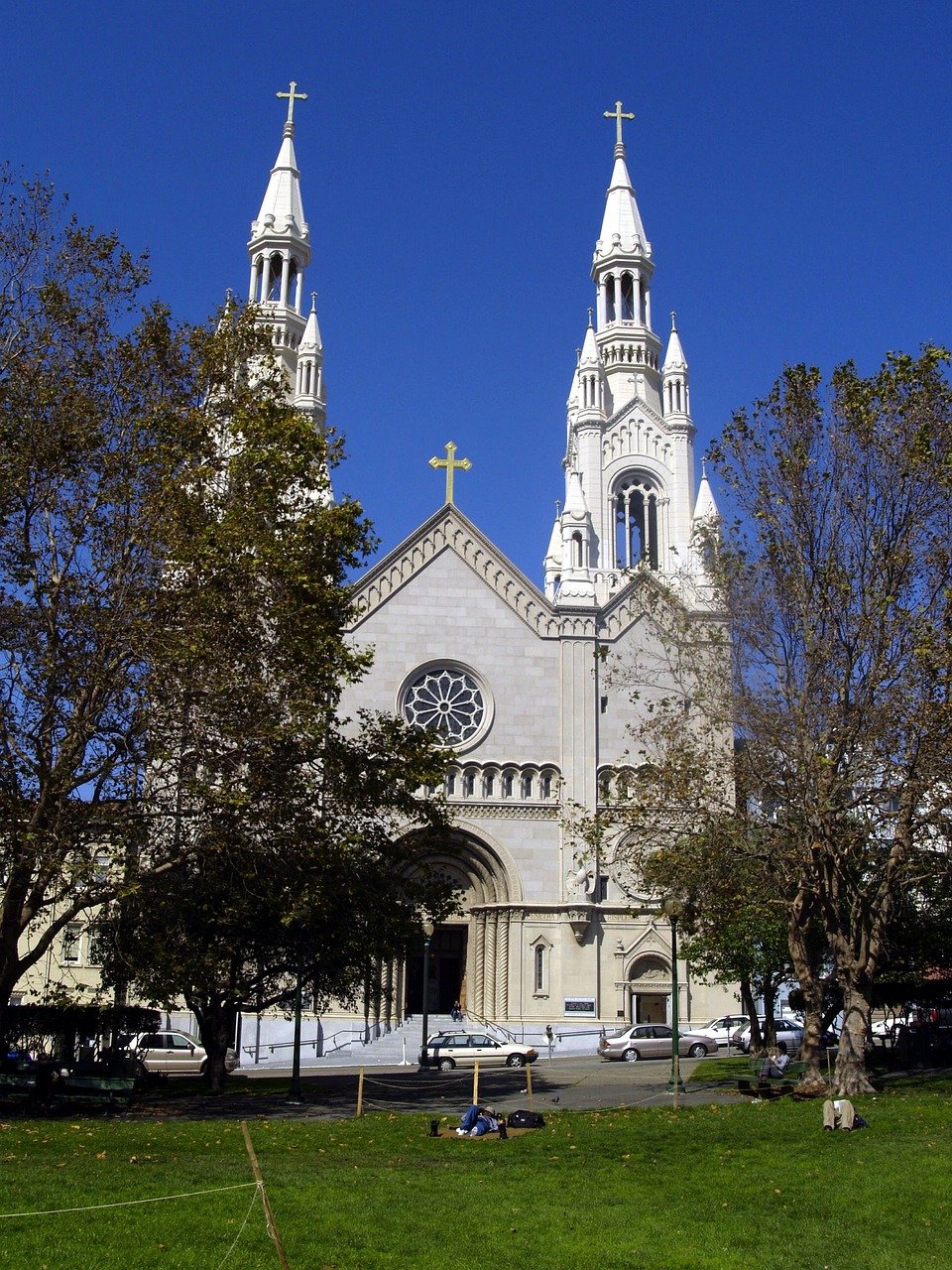 Historic white stone church with twin spires and crosses surrounded by trees under clear blue sky