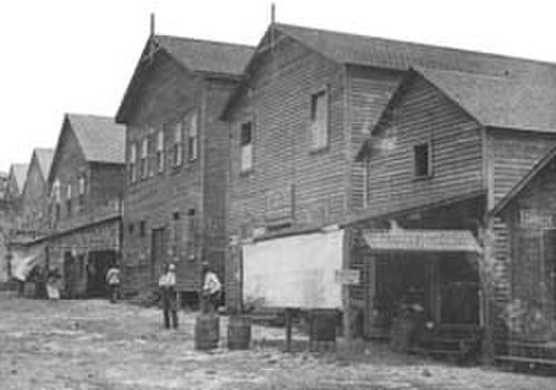 Early 20th Century Wooden Industrial Warehouses Historic black and white photo of old wooden industrial warehouses with workers outside in early 20th century
