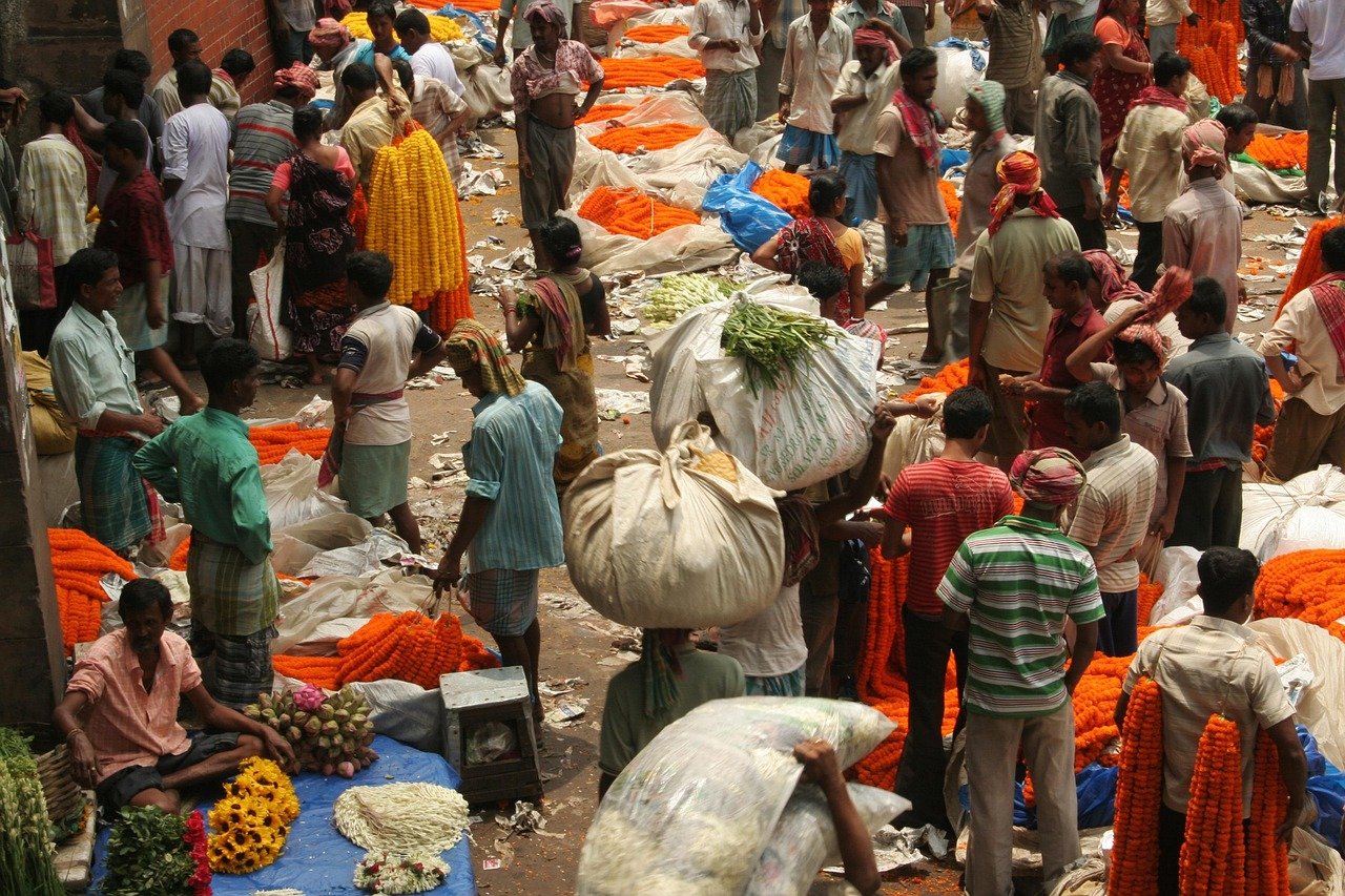 Busy Indian flower market with vendors and buyers surrounded by vibrant orange marigold garlands and fresh flowers