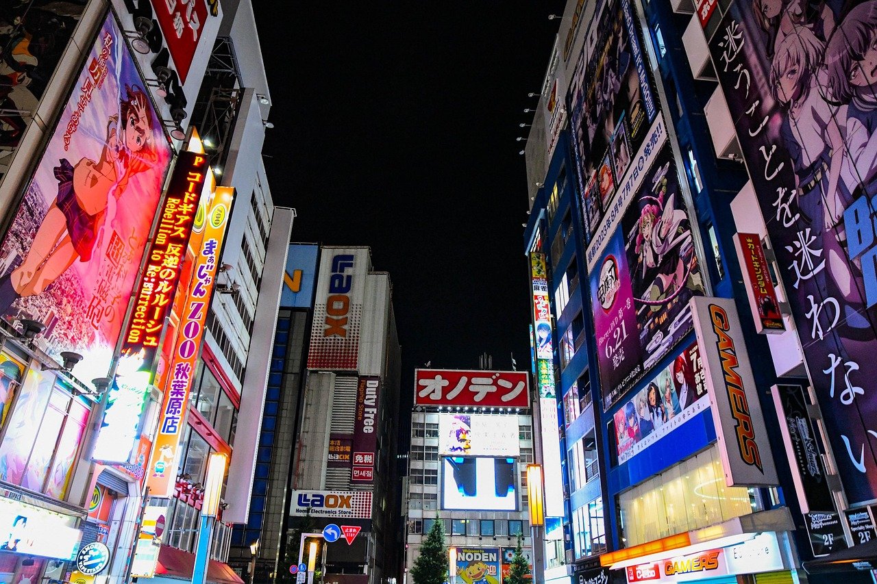 Night view of a busy urban street in Japan with illuminated anime billboards and colorful advertisements