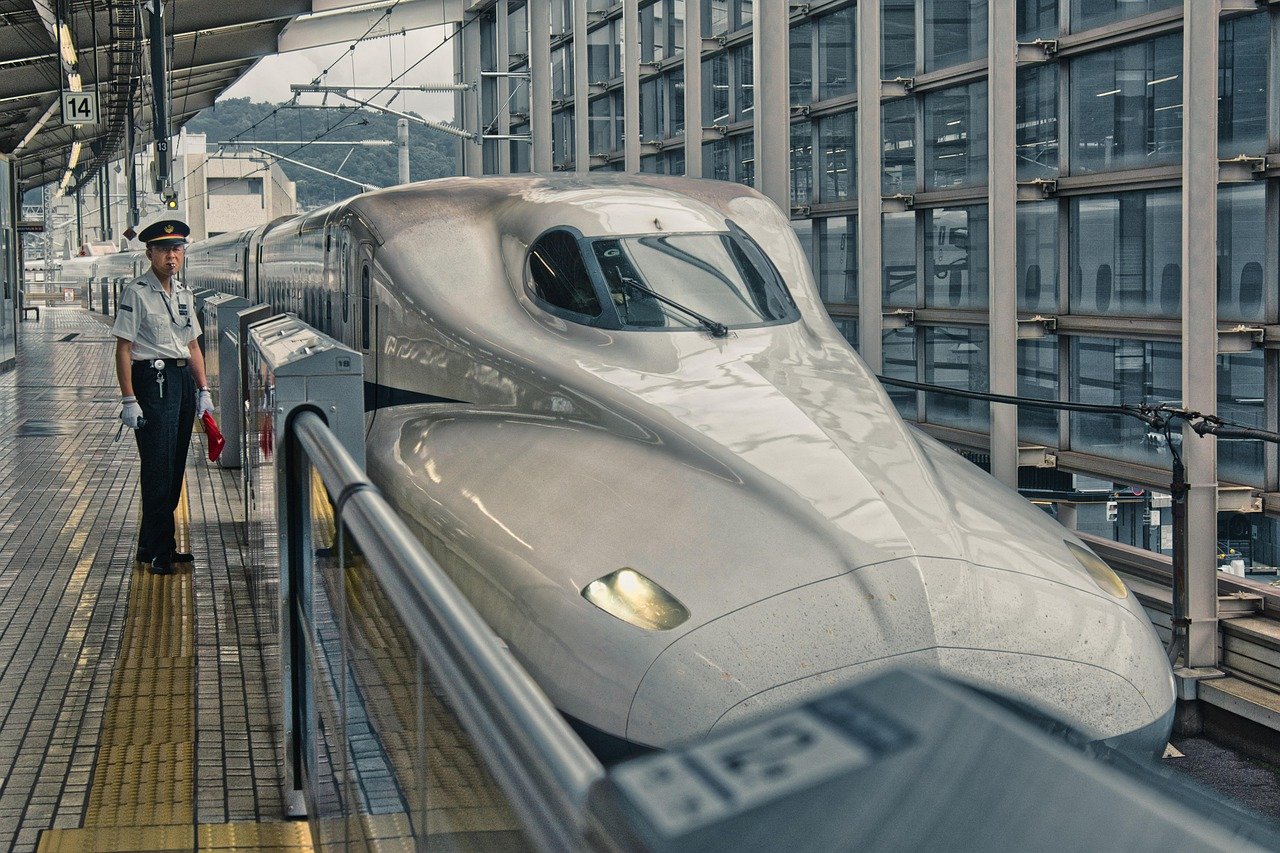 Modern Japanese Shinkansen bullet train at platform with uniformed railway staff in busy station