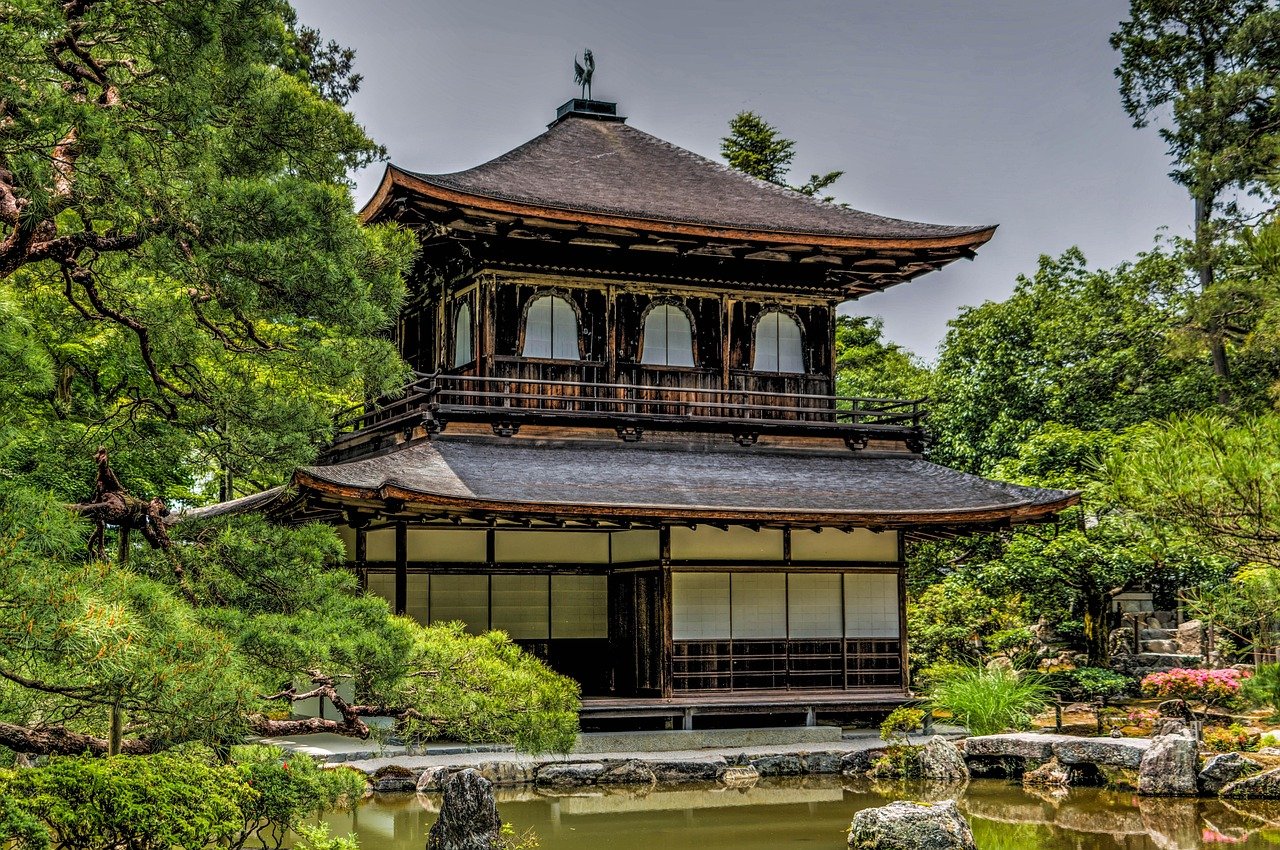 Traditional Japanese wooden temple surrounded by lush green trees and a serene pond in a peaceful garden setting