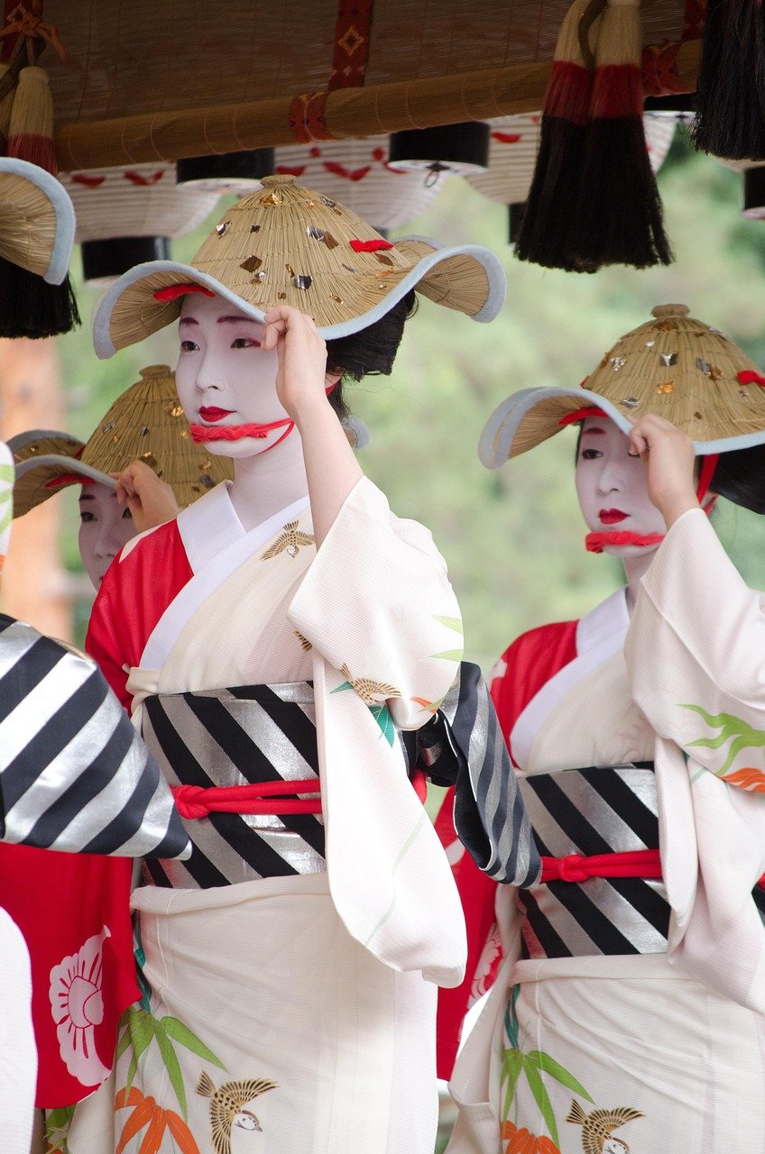 Traditional Japanese women in white kimonos and straw hats performing a cultural dance with painted faces
