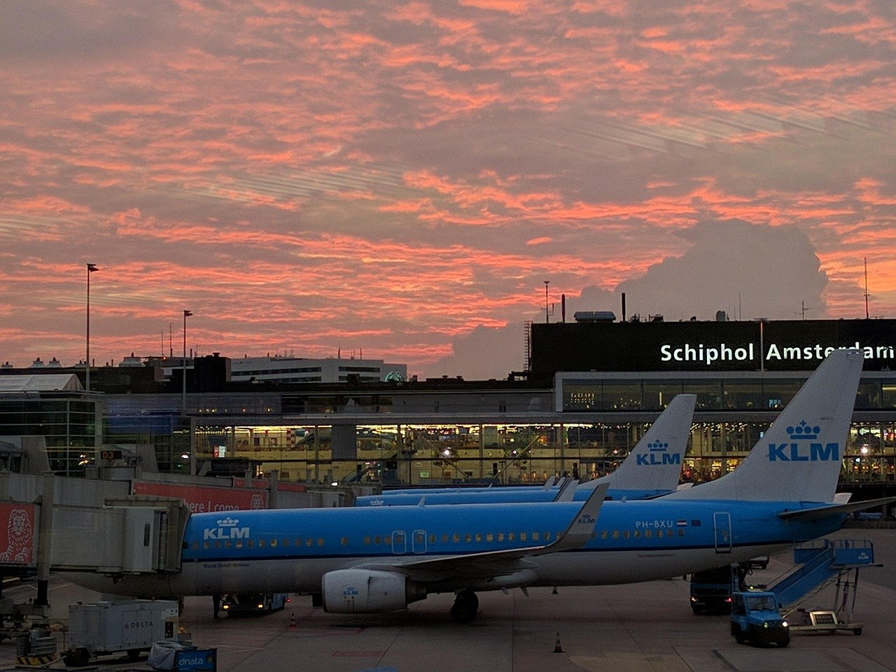 KLM airplanes parked at Schiphol Airport during a vibrant sunset with orange and pink clouds in the sky