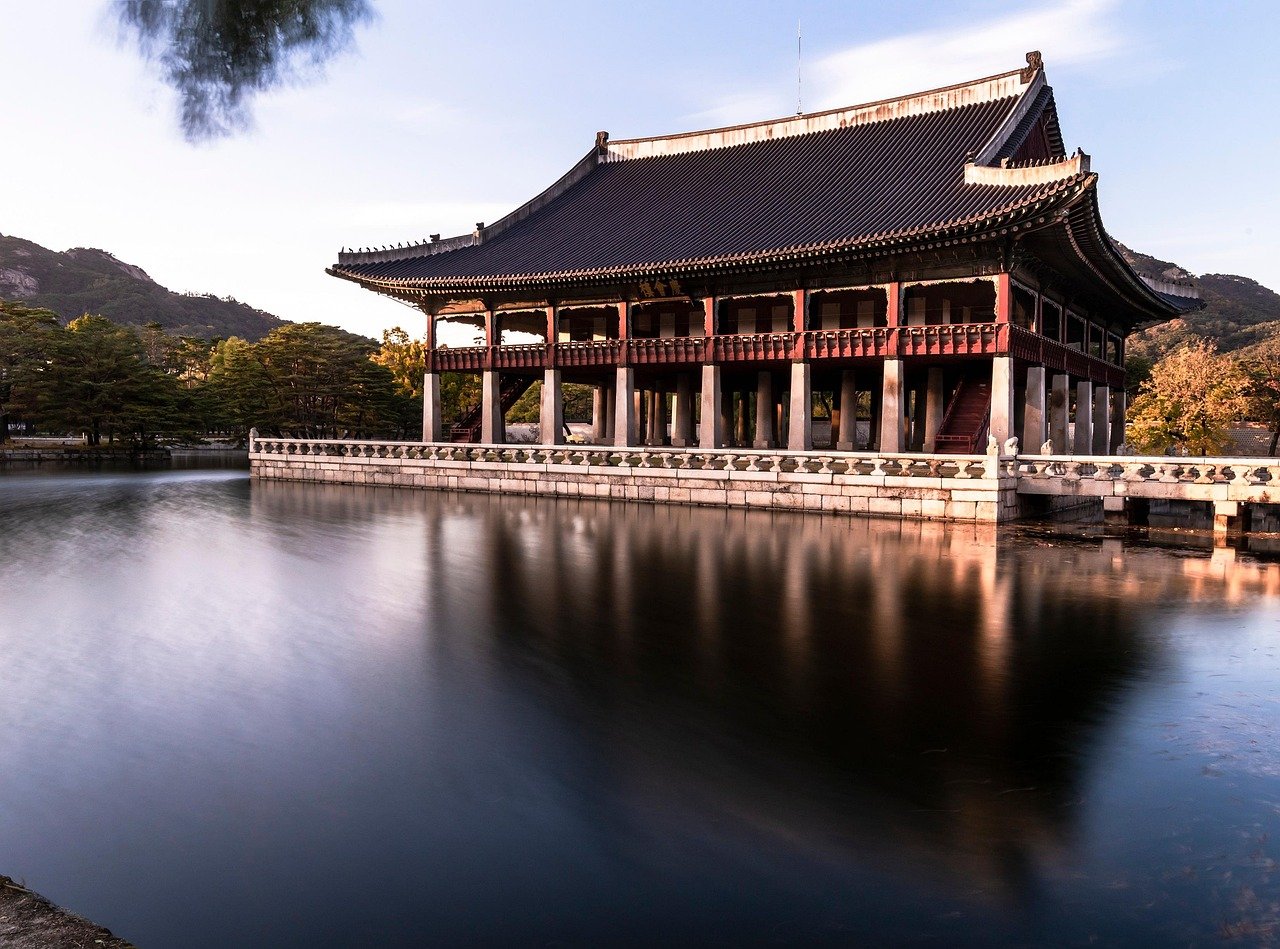 Traditional Korean pavilion Gyeonghoeru surrounded by water and trees with mountains in the background