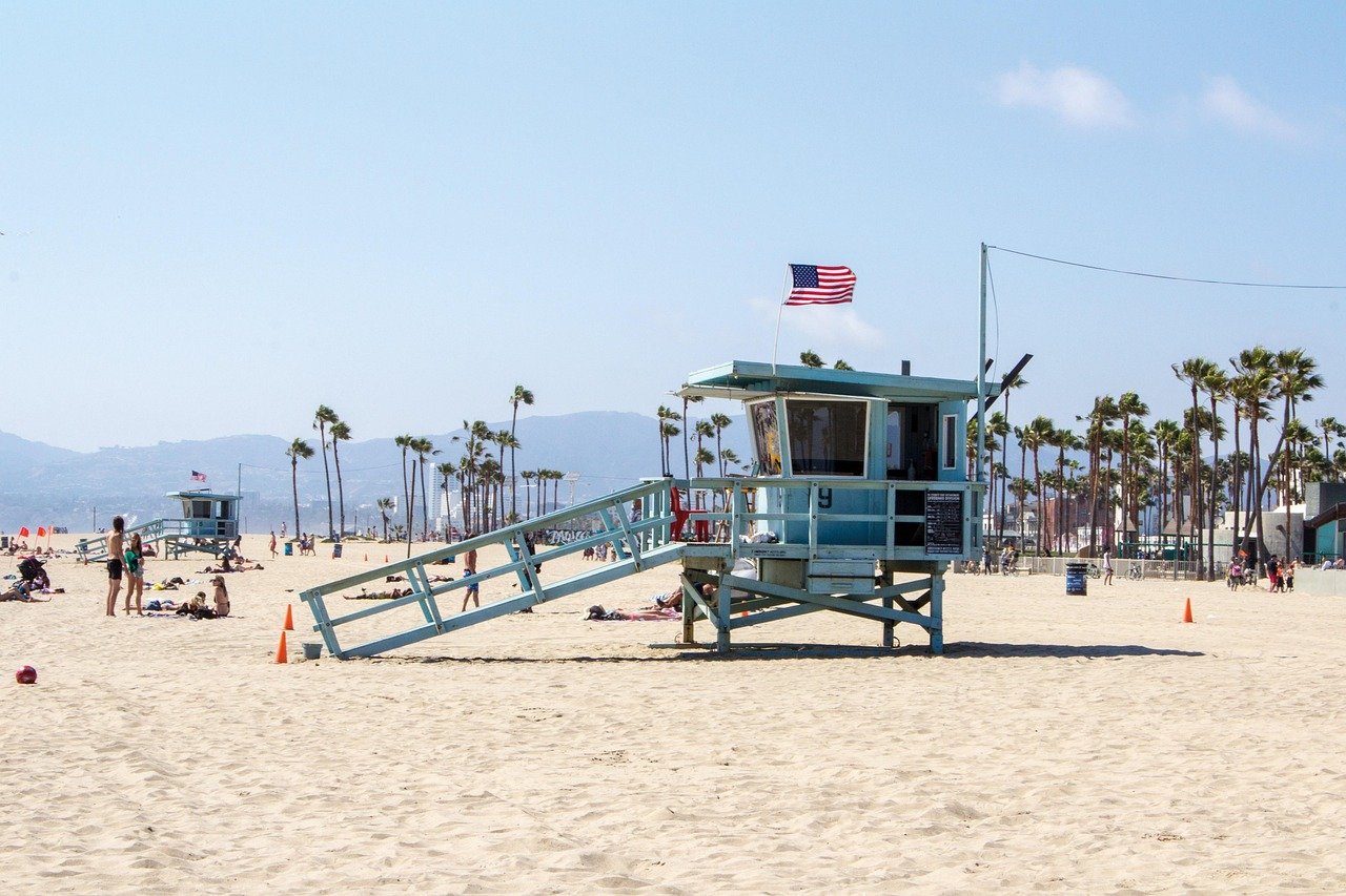 Lifeguard tower on sandy beach with American flag and palm trees under clear blue sky