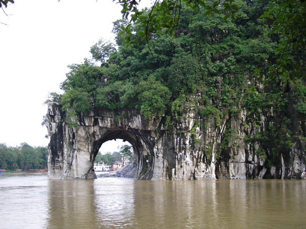 Natural limestone arch formation covered with green vegetation over a river in a scenic landscape