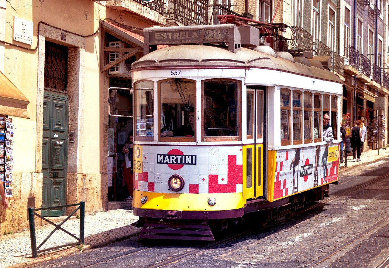 Vintage yellow and white tram number 28 with Martini advertisement traveling on cobblestone street in Lisbon, Portugal