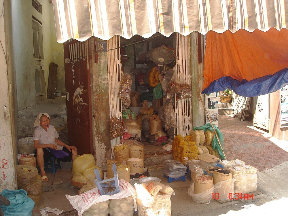 Local market stall with grains and dried goods Small local market stall with various bags of grains, nuts, and dried goods, and a woman sitting on a stool nearby