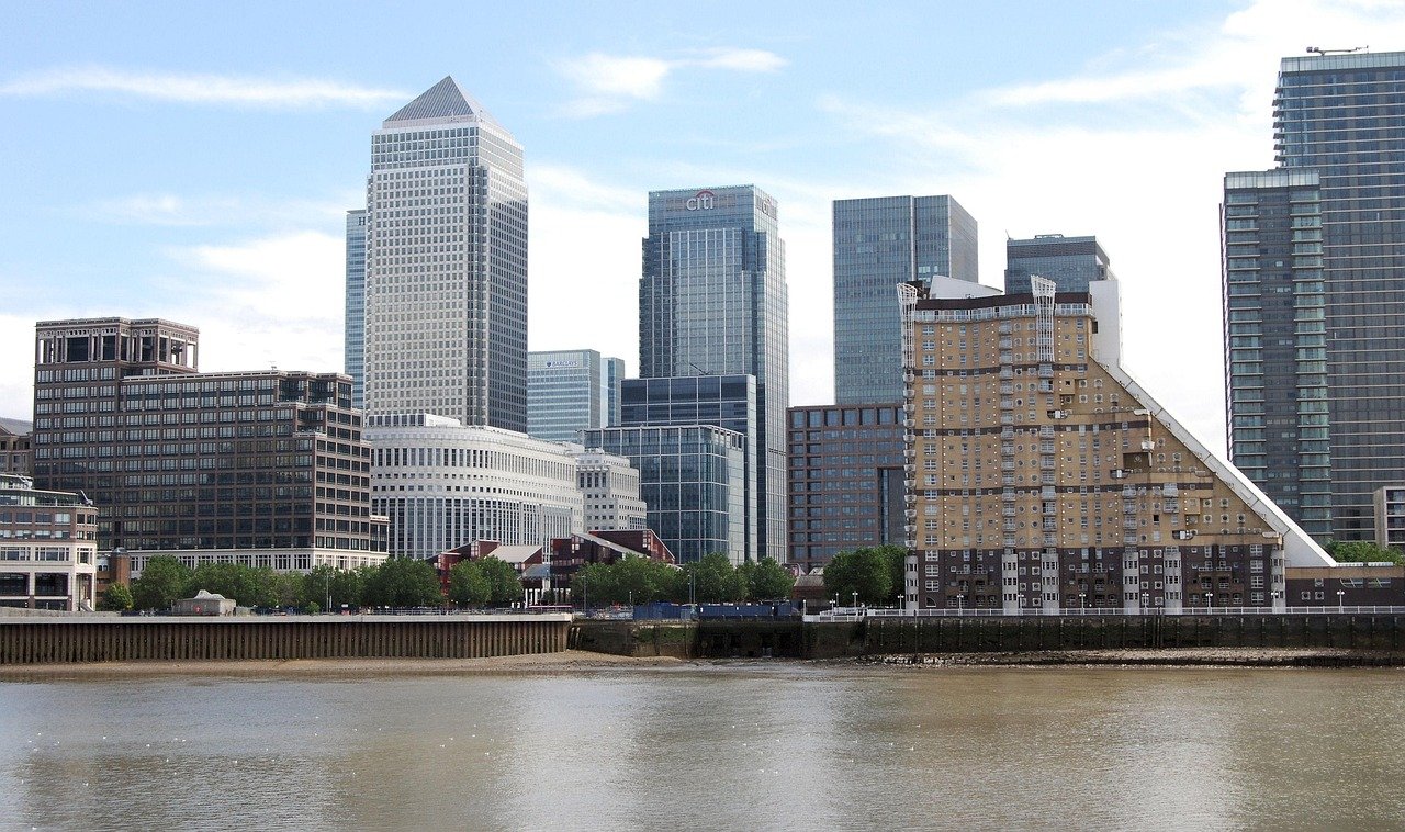 Modern financial district skyline with high-rise office buildings and riverfront in London, featuring Citi and Barclays towers.