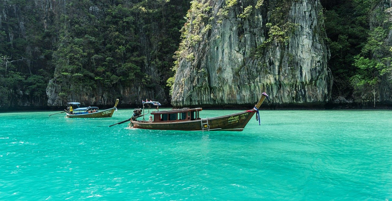Traditional wooden longtail boats floating on clear turquoise water near lush green limestone cliffs in tropical paradise