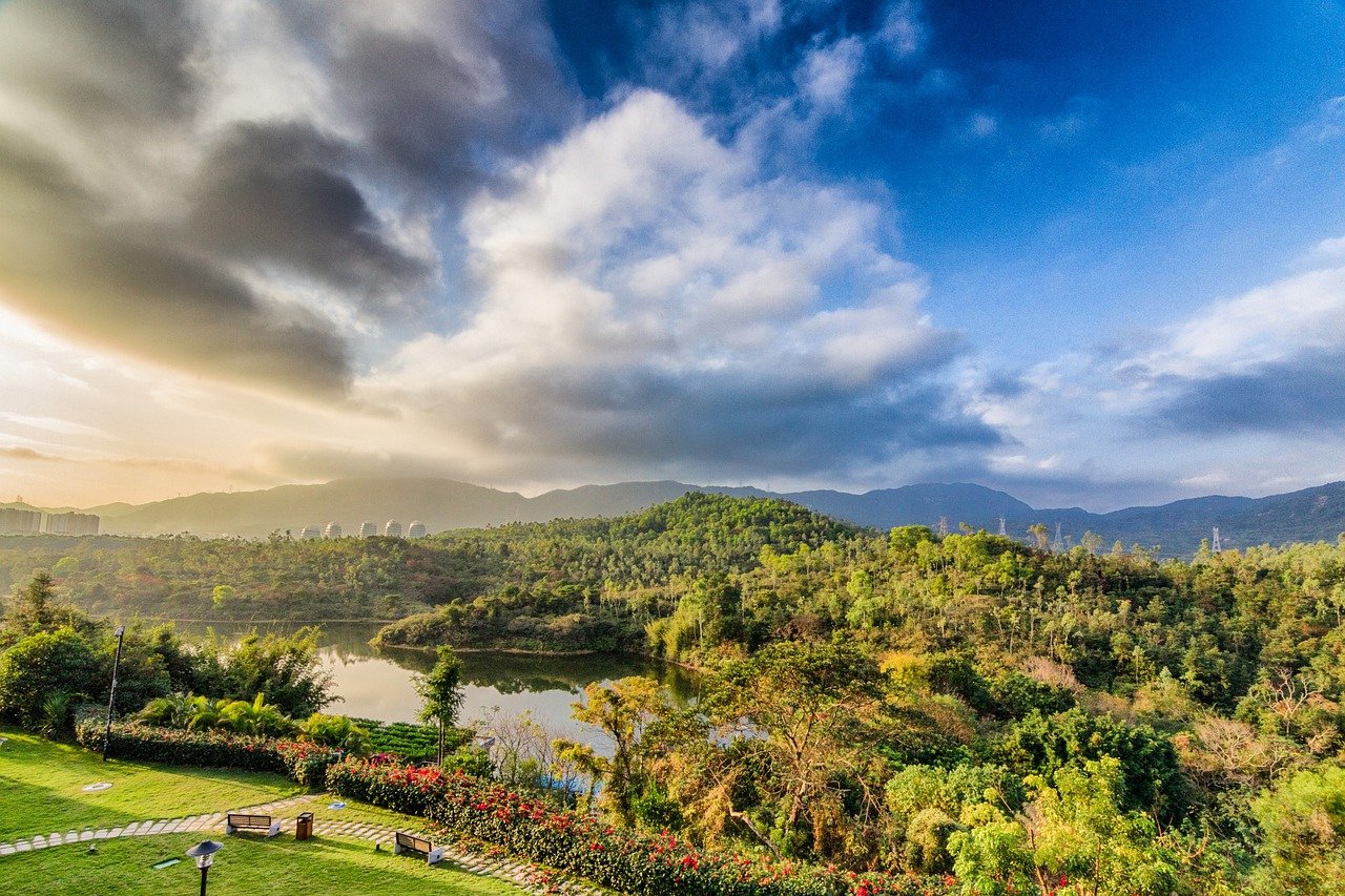 Scenic view of lush green forest, lake, and mountains under a partly cloudy blue sky at sunset
